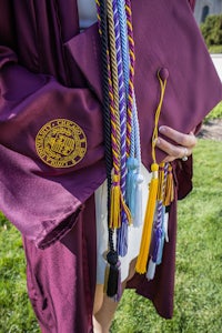 a woman in a maroon cap and gown holding a tassel