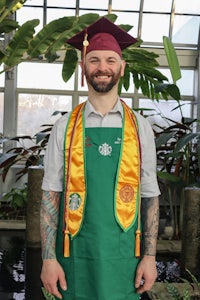 a man in a green apron standing in front of a plant