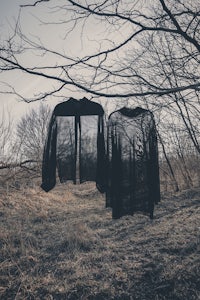 two black jackets hanging on a tree in a wooded area